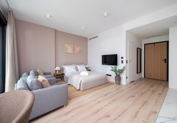 A modern bedroom with a bed, sofa, TV, and a wooden floor.