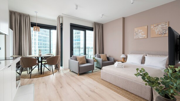 A modern hotel room with a large bed, a dining area with chairs, a sofa, and a view of the city through large windows. - Towarowa Towers 106 Superior Studio (Warszawa)