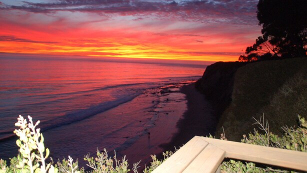 Una puesta de sol sobre una playa con un marco de madera al frente.