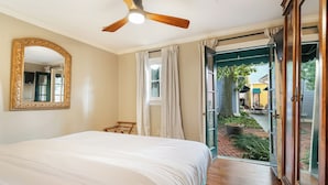 Ein Schlafzimmer mit einem großen Bett, einem Deckenventilator, einem Spiegel und Blick auf die Terrasse.