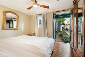 Un dormitorio con una cama grande, un ventilador de techo, un espejo y vistas al patio exterior.
