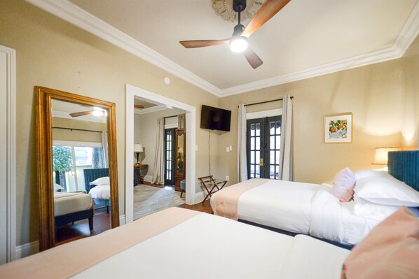 Habitación de hotel con dos camas, ventilador de techo, televisión y un espejo grande.