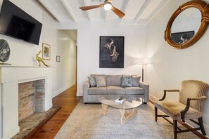 A living room with a sofa, armchair, coffee table, fireplace, TV, and artwork.