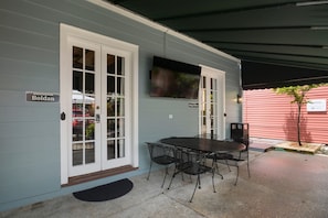 A covered patio with a table and chairs, a television mounted on the wall, and a sign reading "Boldan".