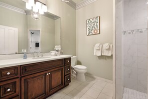 Un baño con tocador de madera, un espejo grande, ducha y un inodoro.