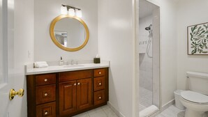 Ein Badezimmer mit einem Holz-Waschtisch, einem runden Spiegel mit Beleuchtung, einer weißen Toilette und einer Duschkabine.