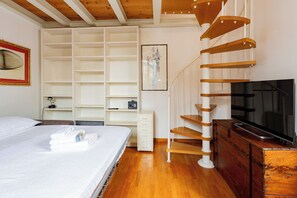 A bedroom with a bed, a TV, a wooden spiral staircase, and built-in shelves.