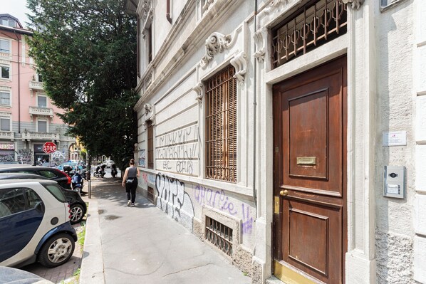 A street view with parked cars, a building with a large wooden door, and graffiti on the wall.