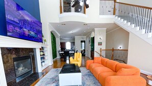 A spacious living room with a fireplace, a large TV, and a staircase leading to an upper level. - Immersive Themed Stay | Space, Jungle & Greek-Inspired Getaway! (Houston)