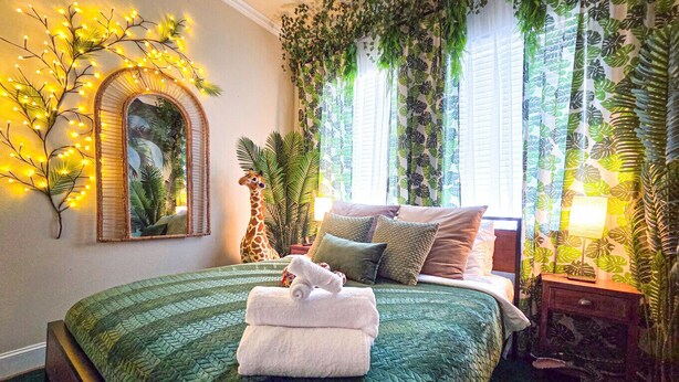 A bedroom with a green quilted bedspread, a mirror, and a giraffe statue. - Immersive Themed Stay | Space, Jungle & Greek-Inspired Getaway! (Houston)