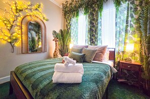 A bedroom with a green quilted bedspread, a mirror, and a giraffe statue. - Immersive Themed Stay | Space, Jungle & Greek-Inspired Getaway! (Houston)