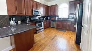 A kitchen with wooden cabinets, a granite countertop, stainless steel appliances, and a wooden floor. - Immersive Themed Stay | Space, Jungle & Greek-Inspired Getaway! (Houston)