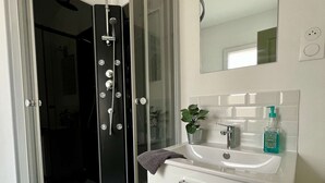 Ein Badezimmer mit Eckbadewanne, einer gläsernen Dusche, einem weißen Waschbecken mit Spiegel darüber und einer Topfpflanze auf der Ablagefläche.