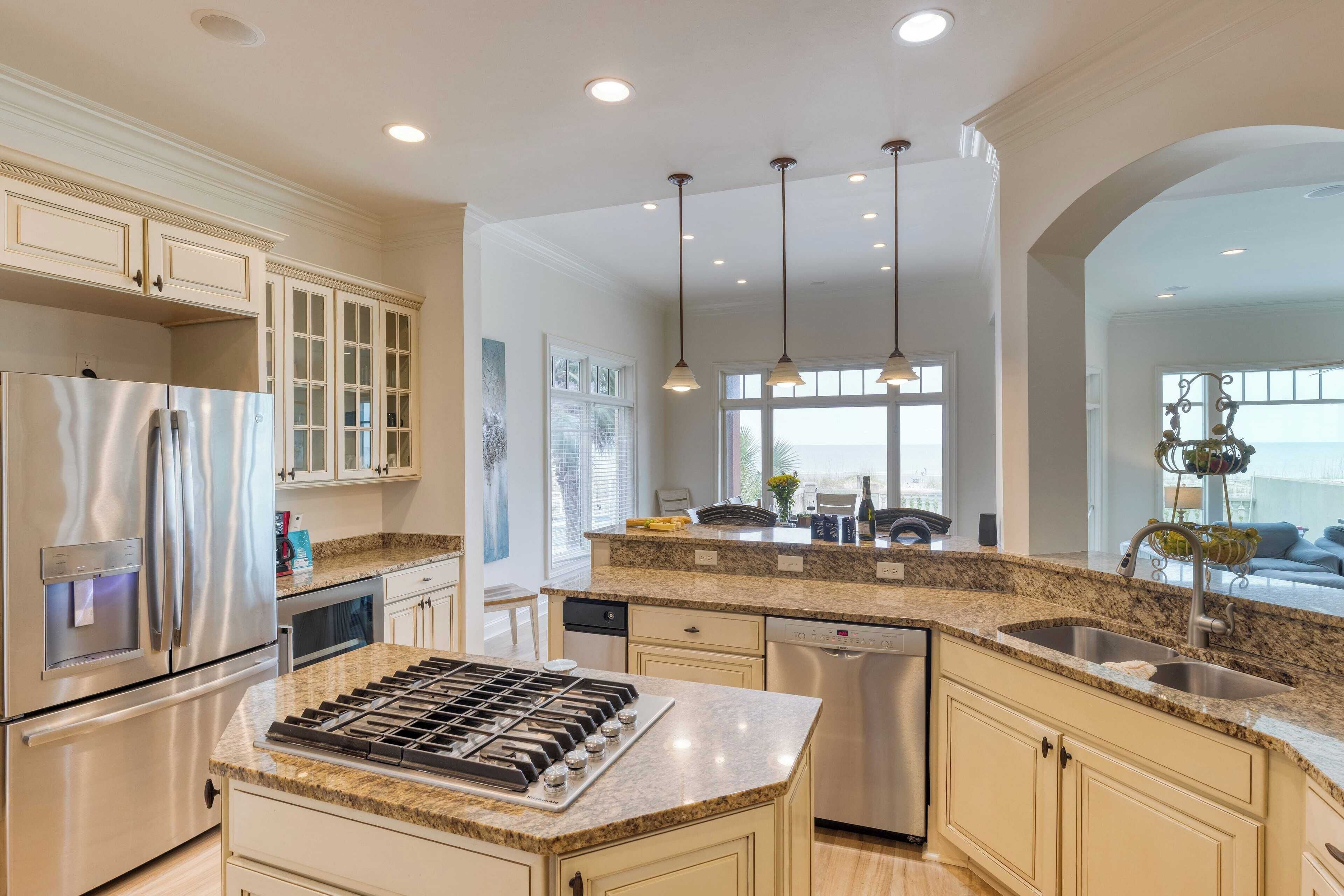 A modern kitchen with a stainless steel refrigerator, built-in oven, granite countertop, and a large island with a sink.