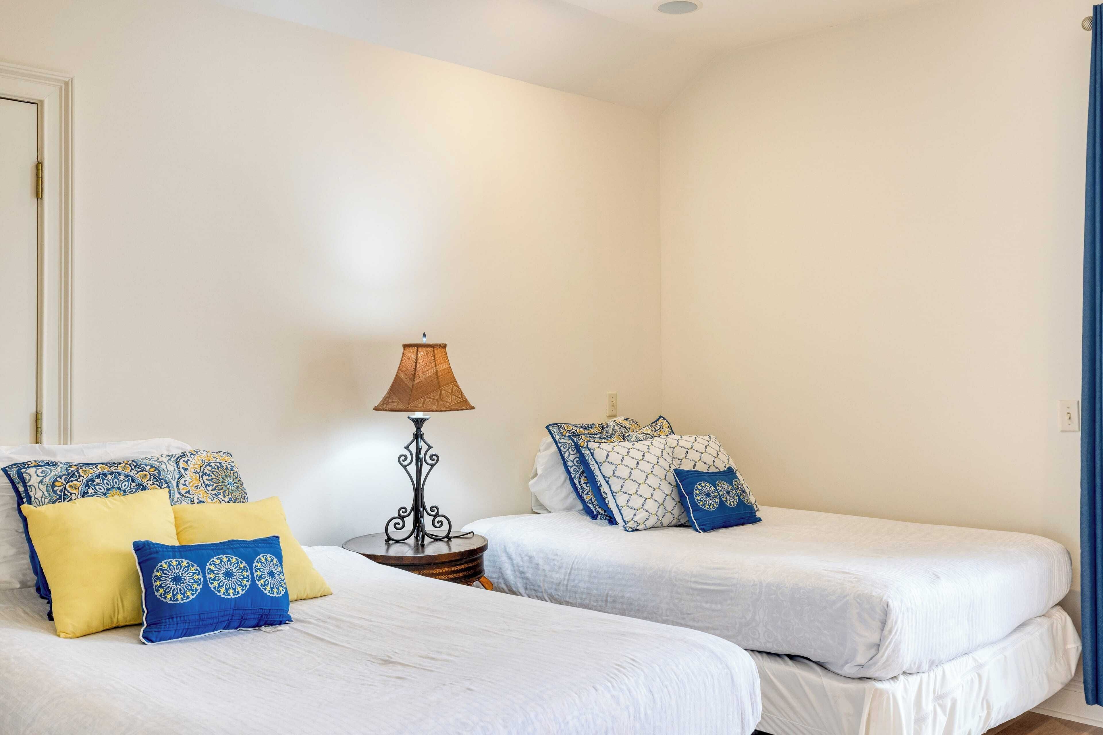 A room with two beds, each with patterned pillows and a lamp between them.