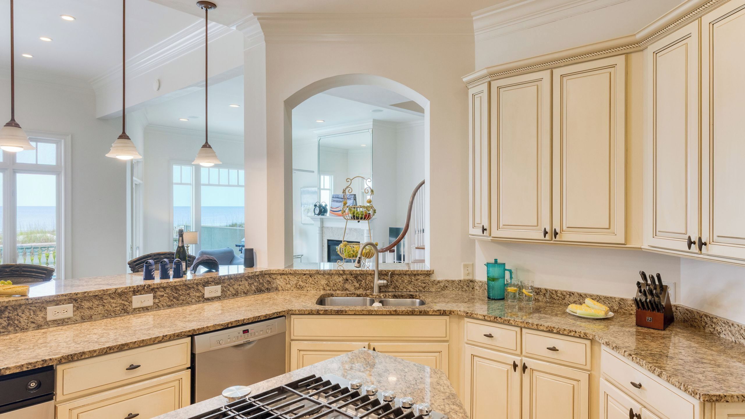 A kitchen with a granite countertop, stainless steel sink, and white cabinetry.