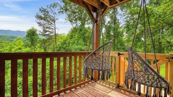 Una terraza de madera con columpios de macramé con vistas a un paisaje boscoso.