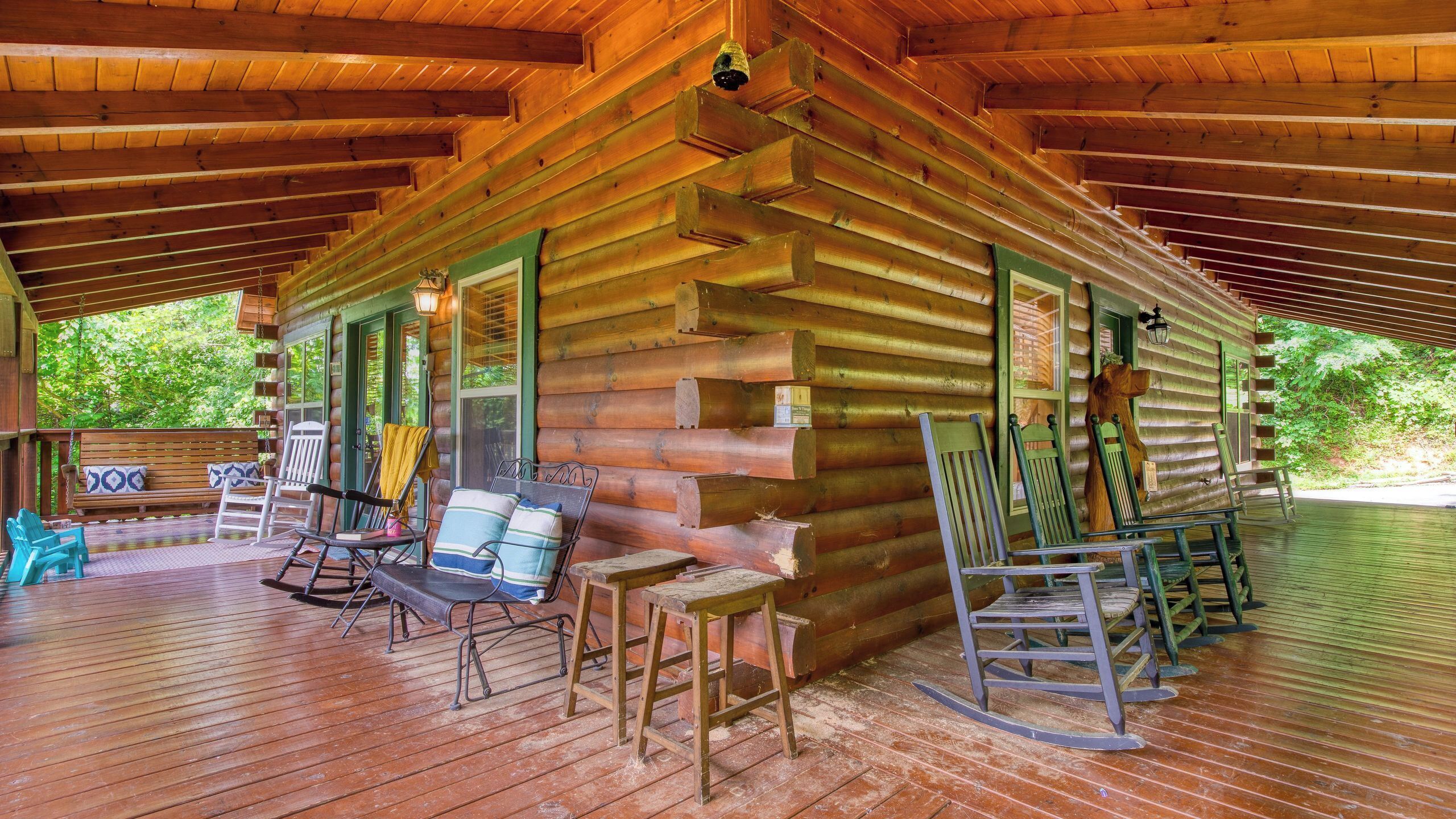 A log cabin with a porch, wooden furniture, and a view of greenery.