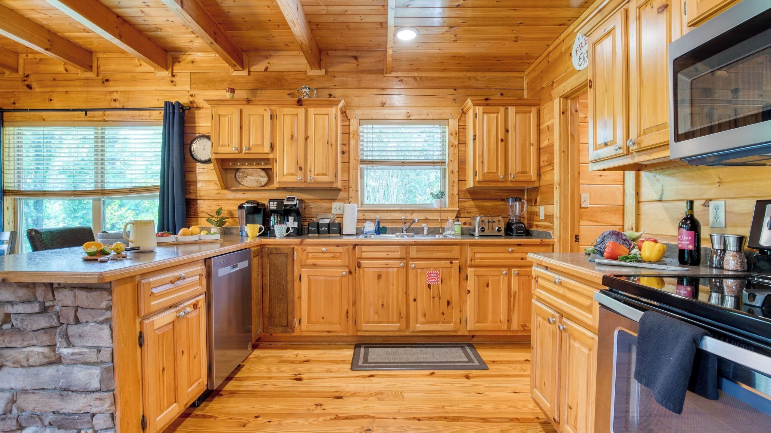 A wooden cabin kitchen with stone walls, wooden cabinets, a stone sink, a stove, and a microwave.