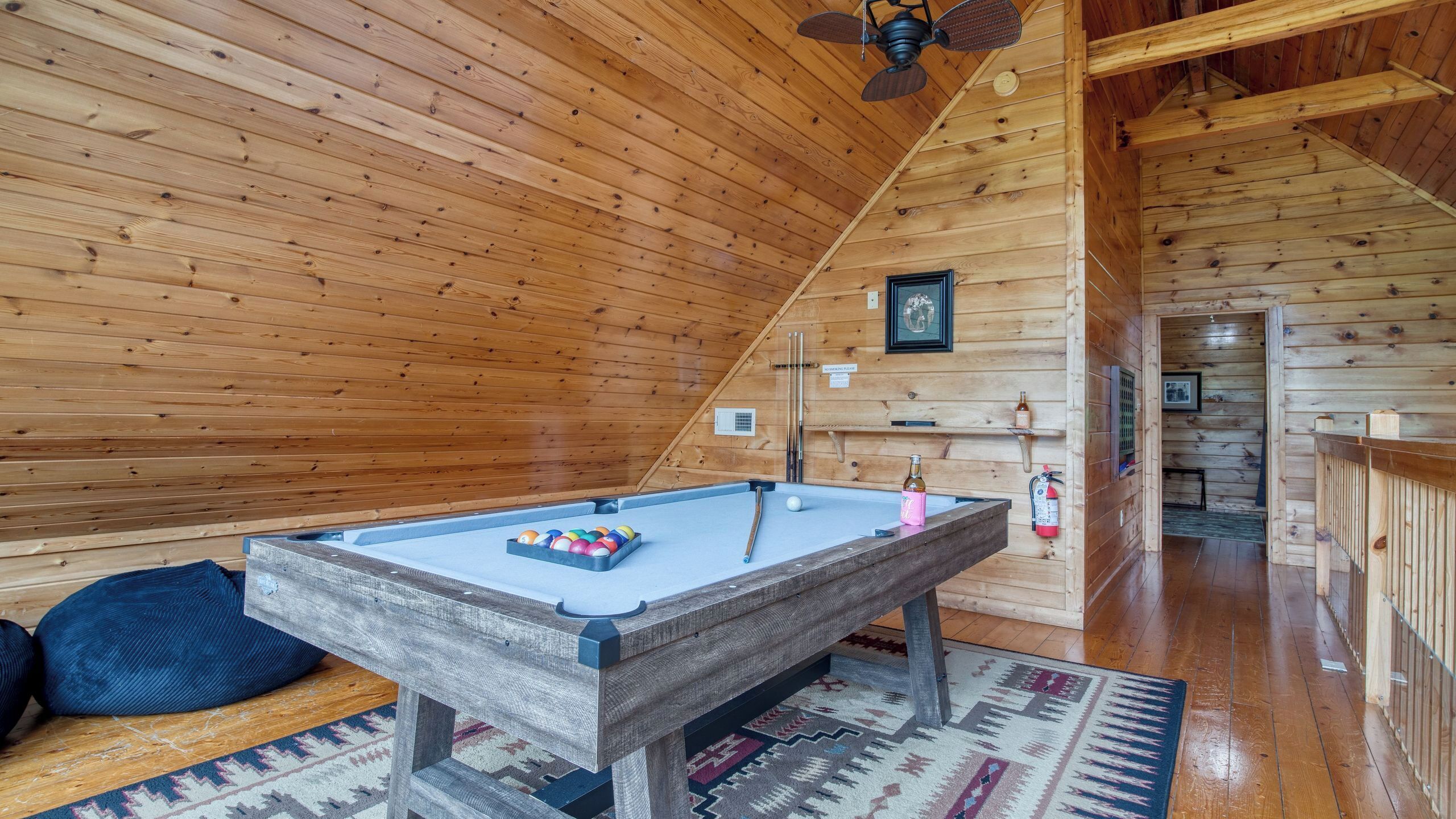 A wooden interior with a pool table, a fire extinguisher, and a ceiling fan.