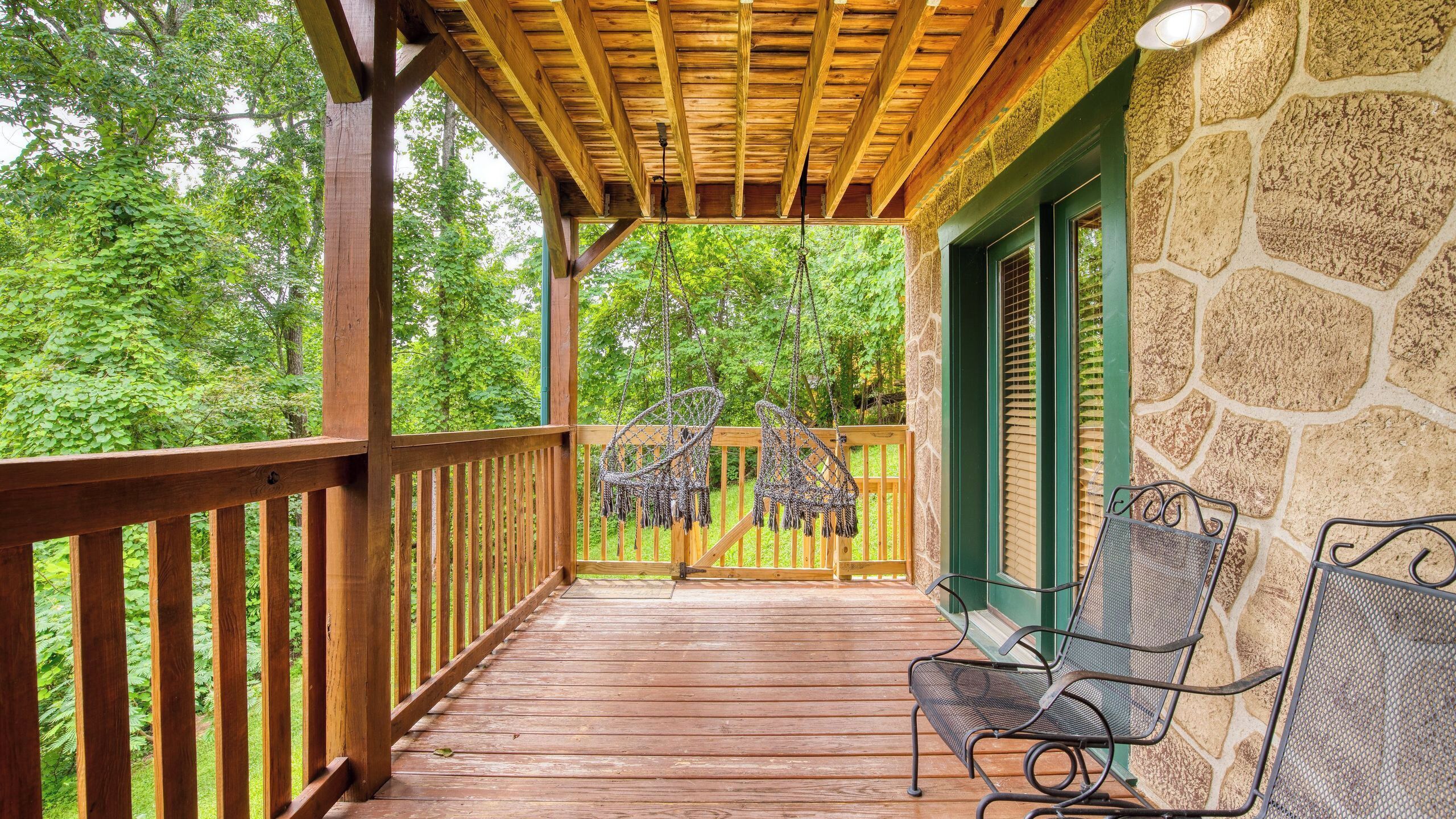 A wooden deck with a stone wall, a bench, and a hanging chair.