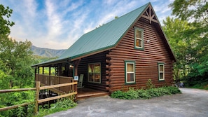 A log cabin with a porch, a covered entryway, and a mountain backdrop.