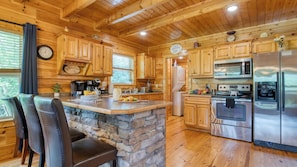 A wooden cabin interior with a stone island, kitchen appliances, and a clock on the wall.