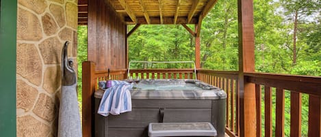 A hot tub under a wooden pergola with stone walls, surrounded by lush greenery.