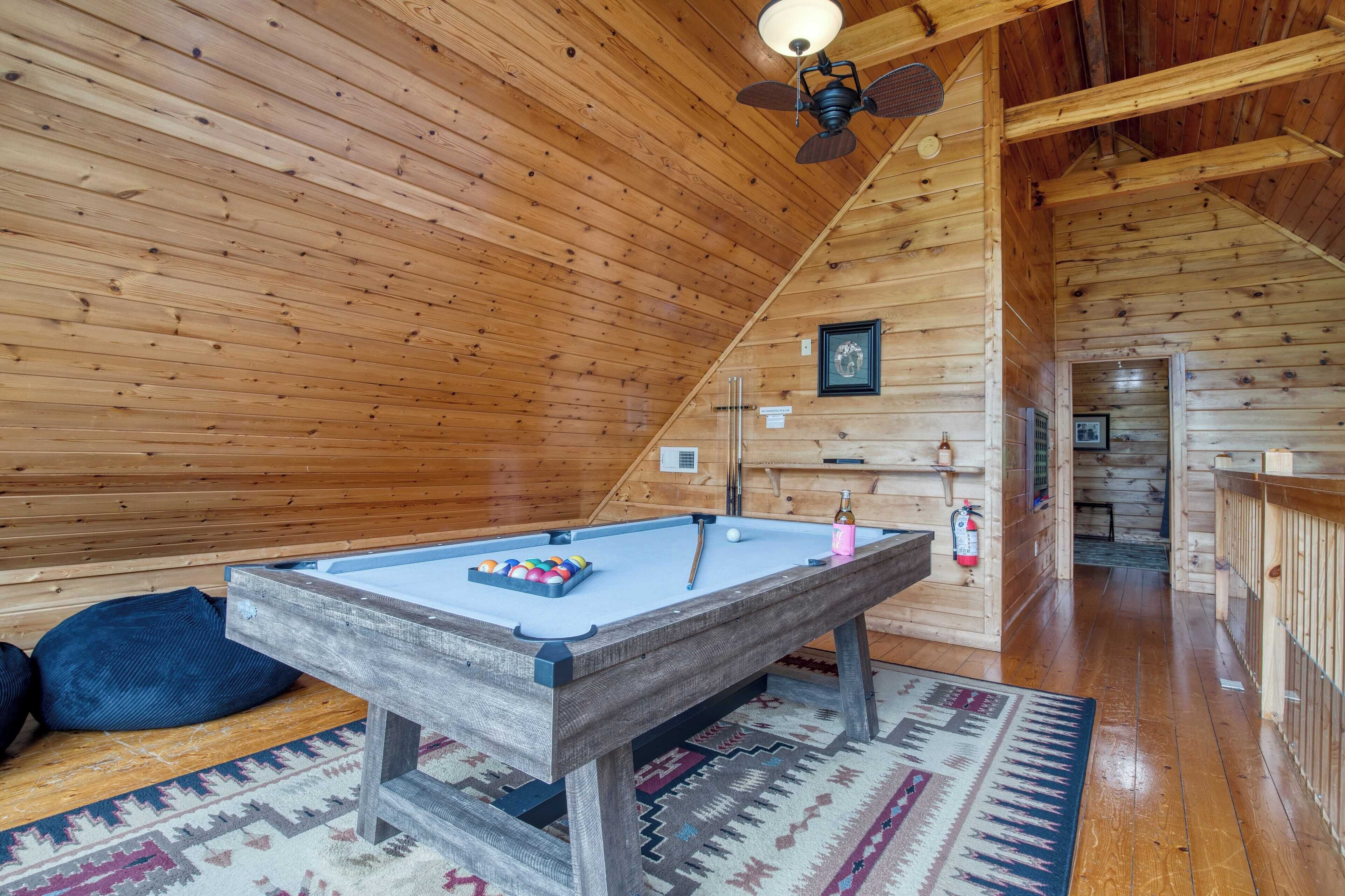A wooden interior with a pool table, a ceiling fan, and a rug.