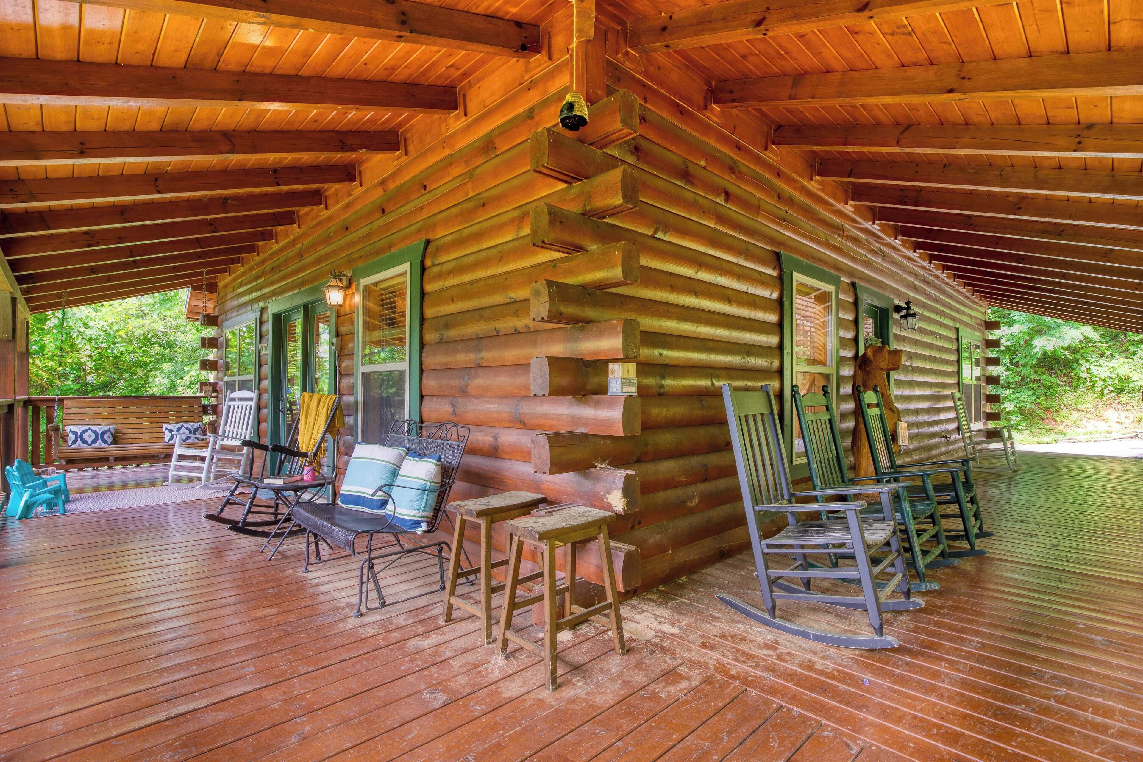 A log cabin with a porch, wooden furniture, and a view of greenery.
