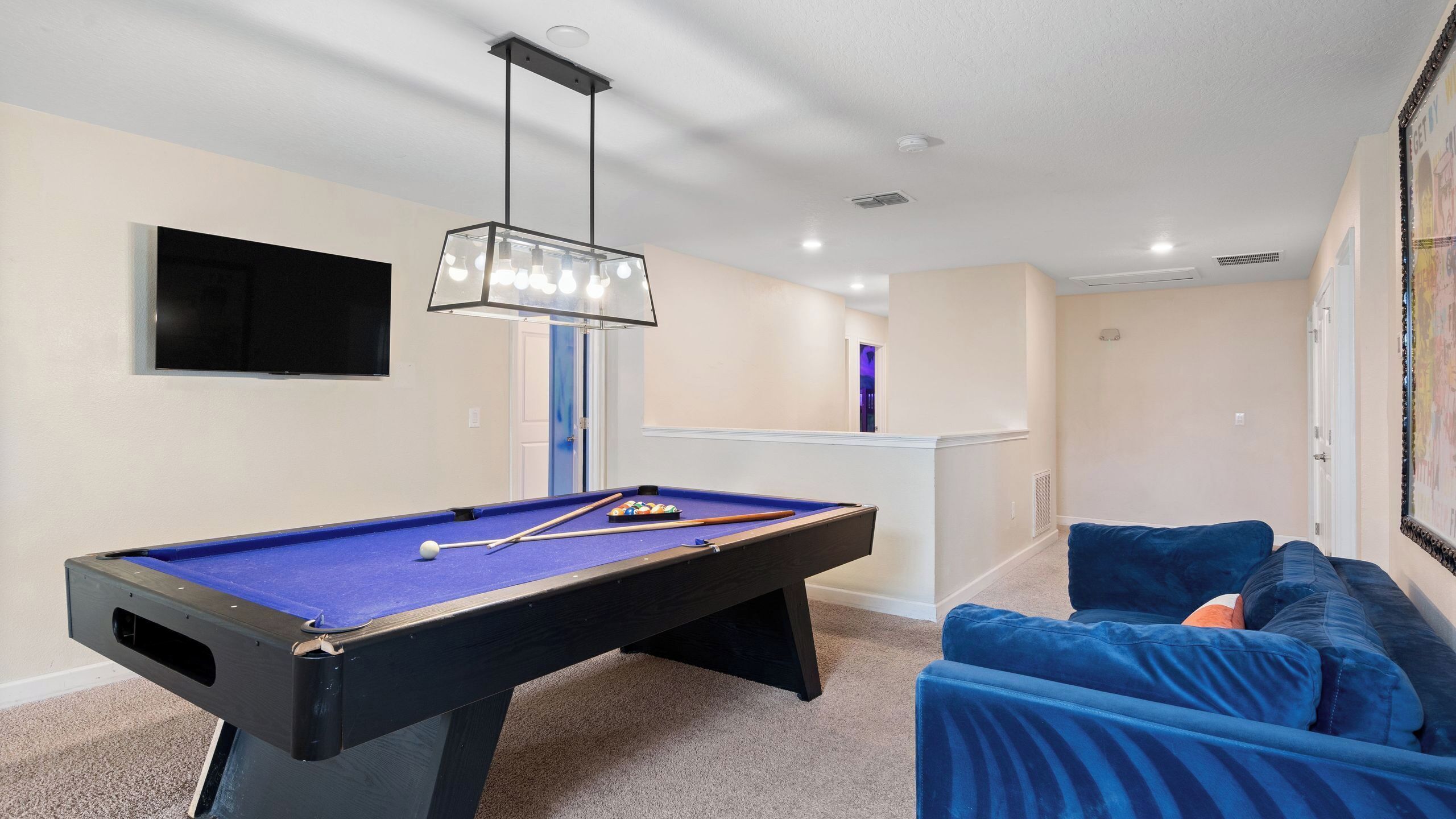 A pool table in a room with a blue sofa, a mounted TV, and a ceiling light fixture.