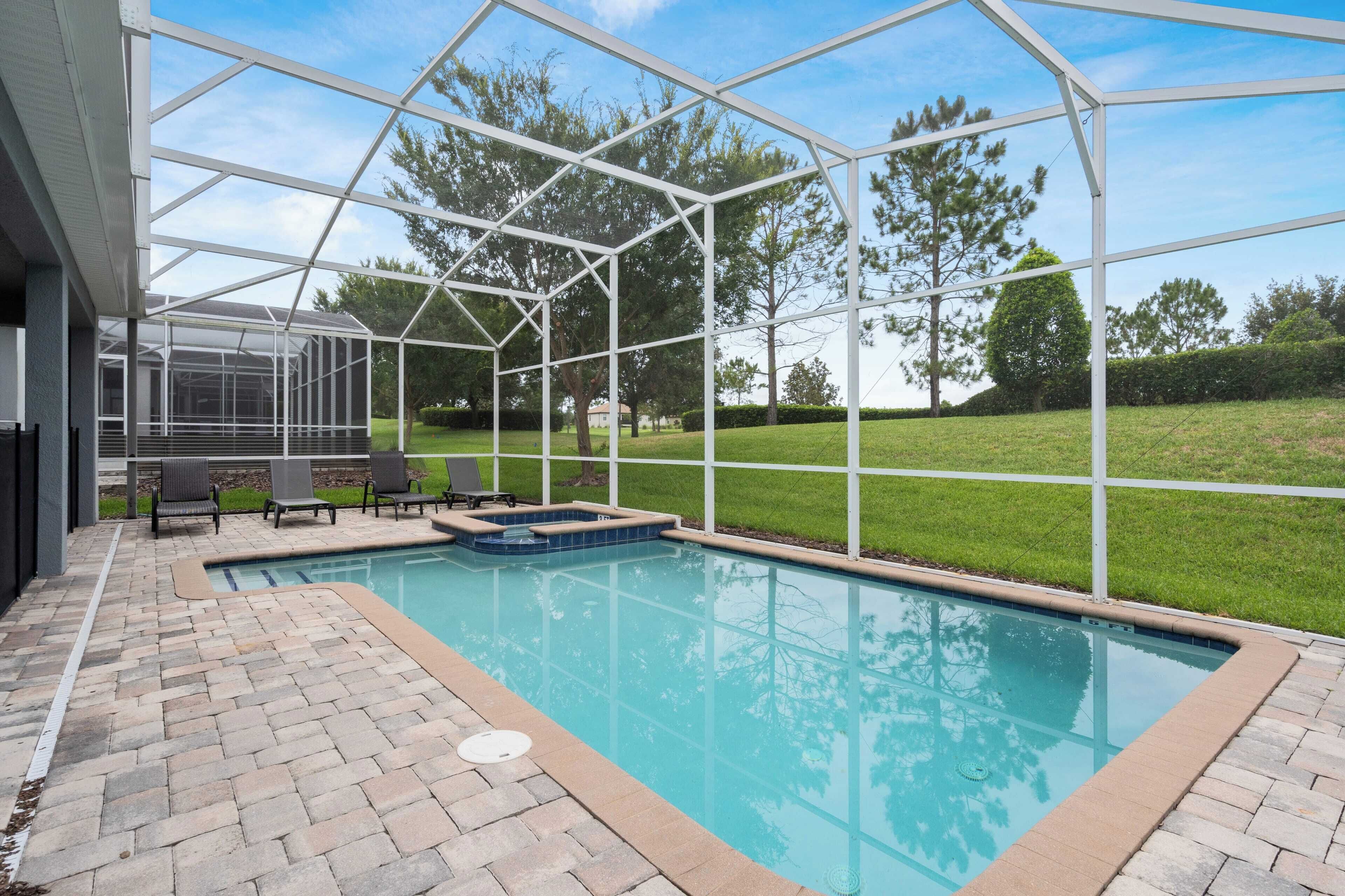 A swimming pool with a glass enclosure, surrounded by a brick patio and outdoor furniture.