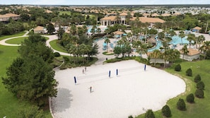 Un terrain de beach-volley avec un filet, entouré de palmiers et un espace piscine avec des chaises longues.