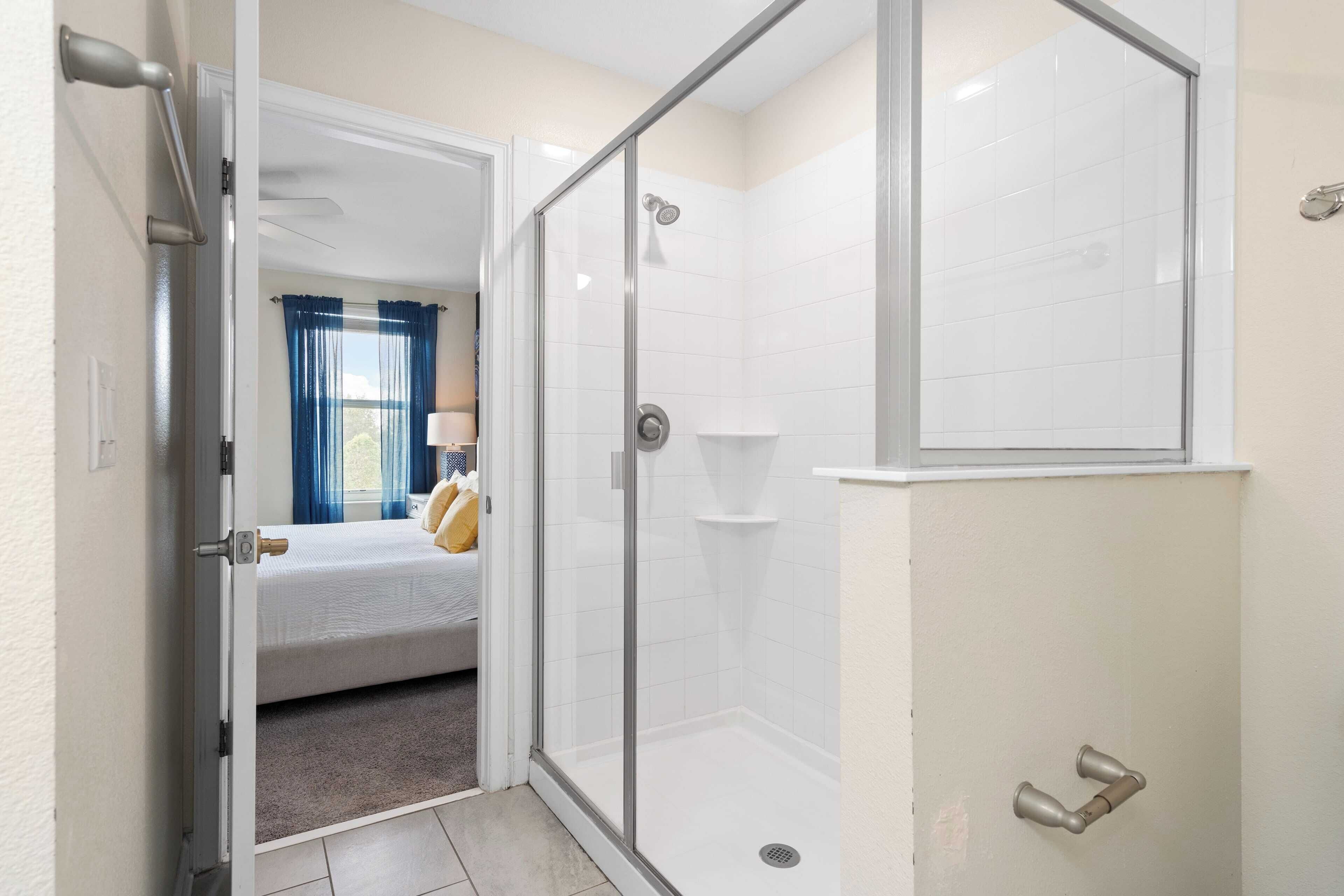 Ein Hotelzimmer mit einer Glaskabine zur Dusche, einem Bett und Blick ins Freie durch ein Fenster mit blauen Vorhängen.