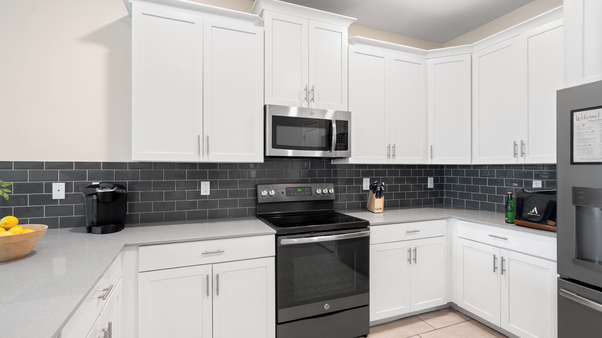A modern kitchen with white cabinets, a black tiled backsplash, a GE stove, a microwave, and a coffee maker.