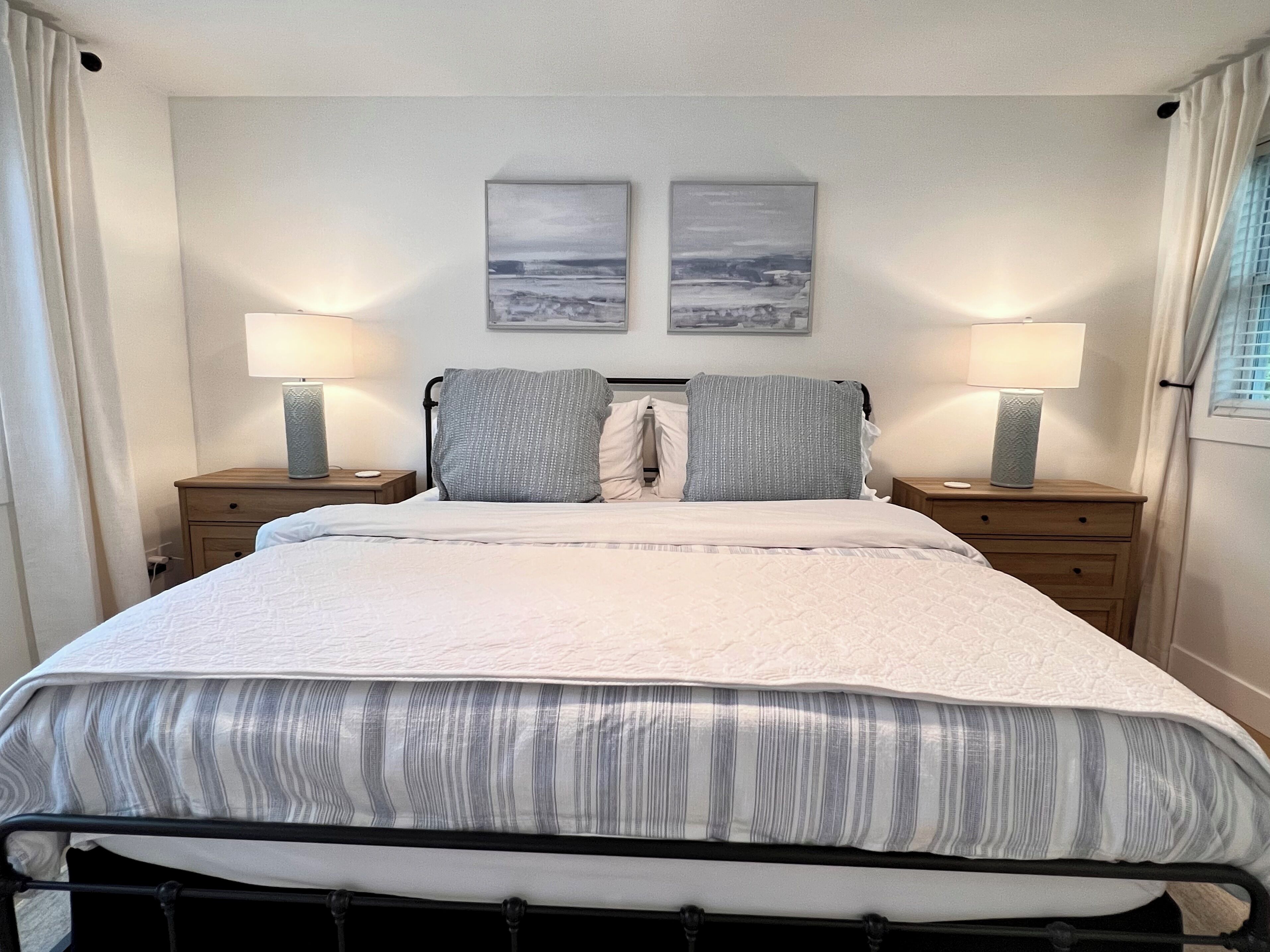 A neatly made bed with a striped bedspread, two pillows, and two bedside tables with lamps.
