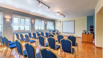A conference room with rows of blue chairs, a projector screen, and a wooden cabinet with items on top.