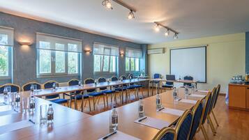 A conference room with long tables, chairs, and a projector screen.