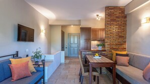 A modern living room with a blue sofa, a wooden dining table, and a brick accent wall. - ERATO & KALYPSO split level apartment (60m² for 2-5 people) (Egialia)