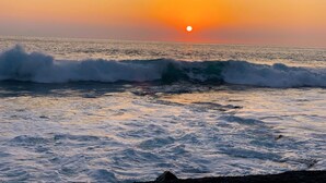 A sunset over the ocean with waves crashing onto the shore.