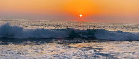 A sunset over the ocean with waves crashing onto the shore.