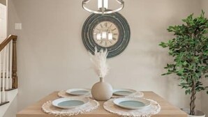 A dining table with four plates and a vase with a feather arrangement, set against a wall with a clock and a potted plant. - Rose District's Coziest Retreat (Broken Arrow)