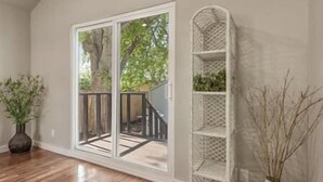 A room with a sliding glass door leading to a deck, a white shelving unit, and a vase with dried plants. - Rose District's Coziest Retreat (Broken Arrow)