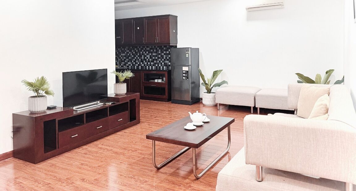 A modern living room with a flat-screen TV, dark wooden entertainment unit, a coffee table, and a light-colored sofa.