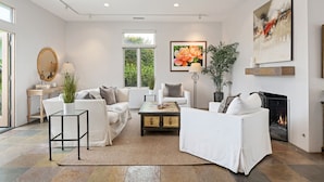 A modern living room with a fireplace, white sofas, a coffee table, and a large painting.