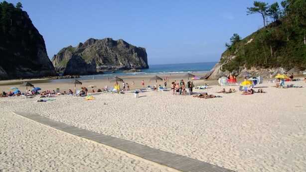 A beach with a wooden walkway, umbrellas, and people relaxing.