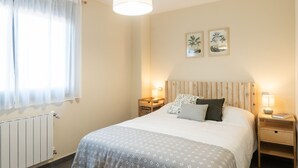 A bedroom with a bed, bedside tables, a radiator, and two wall-mounted pictures.