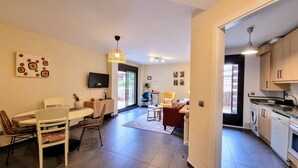 A modern living room with a dining area, a kitchen, and a TV mounted on the wall.