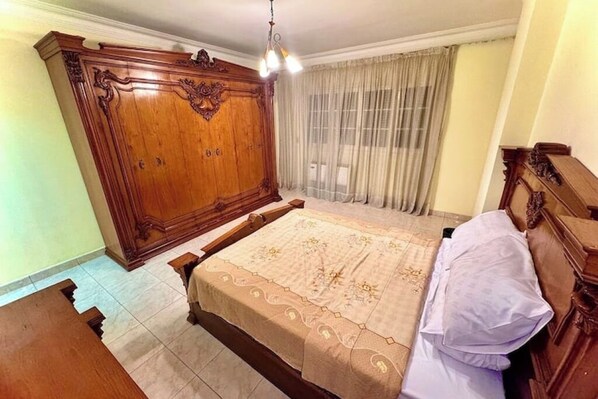 A bedroom with a large wooden wardrobe, a bed with a floral bedspread, and a window with curtains.