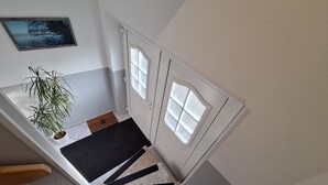 Un escalier avec un tapis noir, une plante en pot et une porte dont les panneaux sont en verre dépoli.